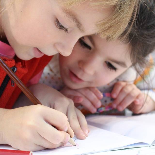 Zwei Grundschulkinder beugen sich über einem Het mit Stift in der Hand