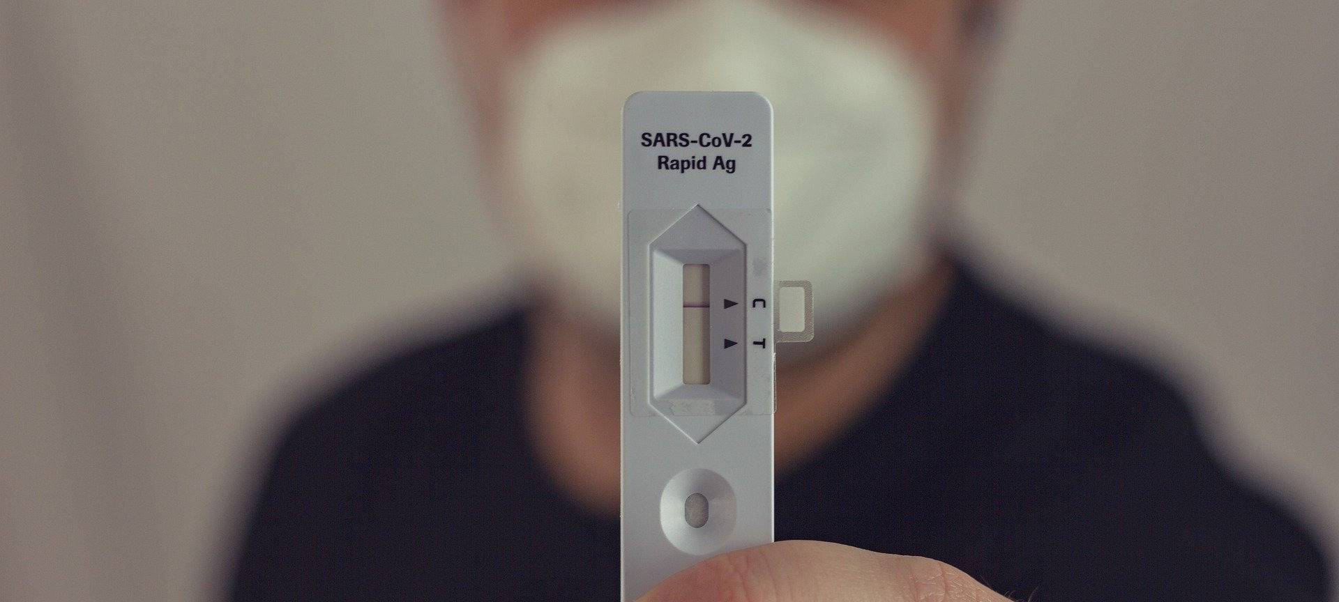 Ein Mann mit einer Schutzmaske hält einen negativen Corona-Schnelltest in der Hand.