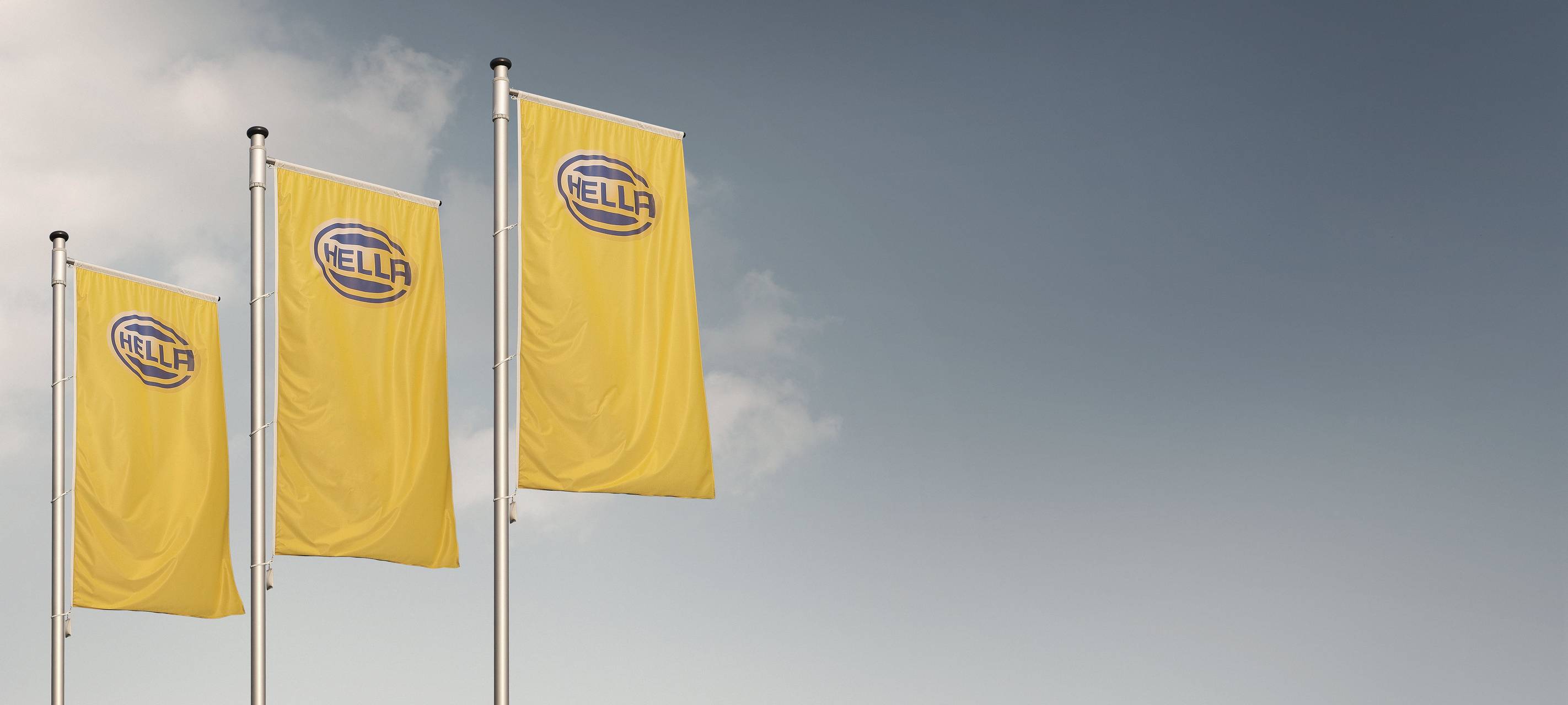 drei Fahnen mit dem Hella Logo blau auf gelben Grund