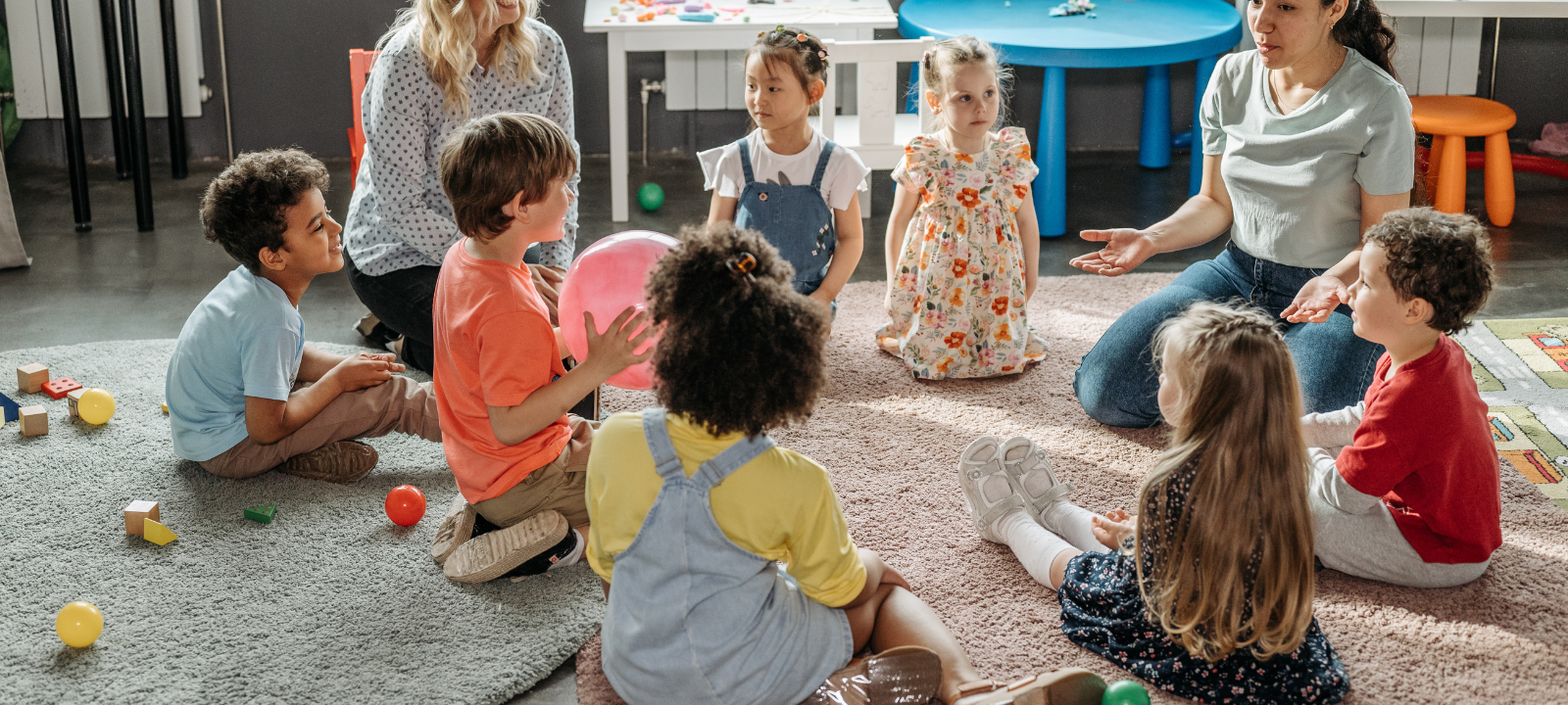 Eine Kita-Gruppe sitzt in der morgendlichen Besprechung mit Erzieherinnen.